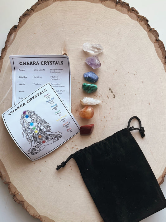 Set of chakra crystals on a wooden surface with a card and black drawstring bag.