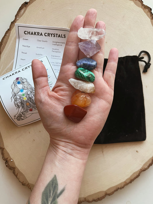 Hand holding a set of chakra crystals with corresponding cards on a wooden surface.